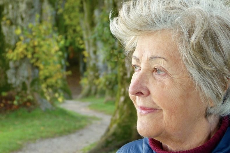 głowa starszej uśmiechnietej kobiety z siwymi włosami na tle zieleni