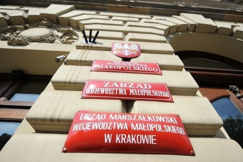 trzy czerwone prostokątne tabliczki z białymi literami, na jednej z nich jest napis Urząd Marszałkowski Województwa Małopolskiego