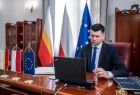 Wicemarszałek Łukasz Smółka siedzi w gabinecie przed komputerem. Obok widoczne flagi Małopolski, Polski i Unii Europejskiej. Z tyłu meble.