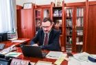 Wicemarszałek Tomasz Urynowicz podczas zdalnego posiedzenia Rady; siedzi przy biurku, patrzy w ekran laptopa; w tle widoczna biblioteczka
