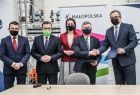 Grupa osób na tle bannerów Małopolski i Grupy Azoty Tarnów. Marszałek Kozłowski i prezes Hinc trzymają teczki z kopiami porozumienia