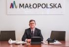 Marszałek Witold Kozłowski siedzi za biurkiem. Na biurku tablet, filiżanka i dokumenty. W tle napis Małopolska.