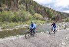 cykliści na rowerach jada drogą szutrową, równolegle do rzeki Dunajec