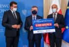 wojewoda Łukasz Kmita, marszałek Witold Kozłowski oraz wójt Stanisław Gorajczyk na tle niebieskiej ścianki i flag, trzymają w ręku czek