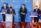 burmistrz Zakliczyna Dawid Chrobak, marszałek Witold Kozłowski - przemawia do mikrofonu, wojewoda Łukasz Kmita, oraz wójt Stanisław Gorajczyk na tle niebieskiej ścianki i flag, trzymają w ręku czek