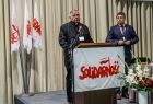 ksiądz oraz Adam Lach przy mównicy, flaga Solidarności