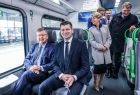 Marszałek Witold Kozłowski i wicemarszałek Łukasz Smółka siedzą w nowym pociągu w kabinie pasażerskiej. Z tyłu widoczni podróżni.