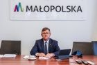 Marszałek podczas posiedzenia zarządu. W tle napis MAŁOPOLSKA. Na biurku dokumenty. Obok stoją krzesła