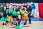 Minister Andrzej Adamczyk stoi na scenie z grupą dzieci. W rękach trzymają kolorowe pompony.