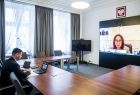 Wicemarszałek Łukasz Smółka siedzi w sali konferencyjnej. Na ekranie wyświetlona kobieta.