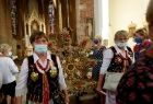 Kobiety w strojach regionalnych wynoszą wieniec dożynkowy z kościoła