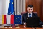 Wicemarszałek Łukasz Smółka siedzi przed monitorem komputera w gabinecie. Na pierwszym planie flagi Polski, Małopolski i Unii Europejskiej.