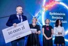 Jeden z laureatów trzyma czek na 10000 złotych i przemawia do mikrofonu na scenie.