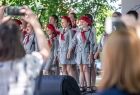 Dzieci w harcerskich mundurach z biało-czerwonymi chustami podziwiane i filmowane przez osoby stojące przed sceną 