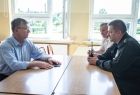 Trzech mężczyzn rozmawia siedząc przy biurkach w sali szkolnej