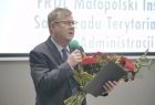marszałek mówi do mikrofonu, trzyma kwiaty