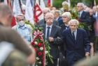 wierni podczas uroczystości pogrzebowych na cmentarzu, w dłoni mężczyzny wieniec