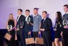 Nagrodzeni sportowcy stoją w rzędzie, trzymając w rękach upominki