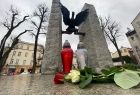 Dwa znicze i kwiaty położone na płycie pomnika. Na pomniku orzeł z rozpostartymi skrzydłami. 