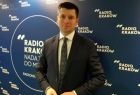 Wicemarszałek Łukasz Smółka w Radio Kraków. Z tyłu widoczna granatowa ściana z białym logo Radia Kraków.