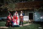 Dwie kobiety i dwóch mężczyzn w strojach folklorystycznych na tle drewnianej chałupy