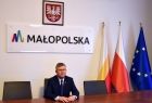 Marszałek siedzi za biurkiem. w tle flagi i napis małopolska