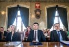 Wicemarszałek Łukasz Smółka podczas otwarcia wydarzenia Senioralia 2021 siedzi na sali obrad. Obok Wioletta Wilińska Dyrektor ROPS w Krakowie i mężczyzna. W tle siedzą w ławach seniorzy.