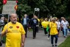 Seniorzy w czasie marszu Senior ma moc. Mężczyzna trzyma transparent z napisem Cukier krzepi starość jeszcze bardziej. Na żółtej koszulce ma napis Medyczny Uniwersytet Trzeciego Wieku.