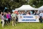 Seniorzy stoją przed namiotem z transparentem z napisem Seniorzy Hrubieszów.