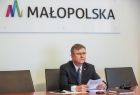 Marszałek Witold Kozłowski podczas wideokonferencji, w tle, na ścianie logo i napis Małopolska