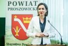 Marta Malec-Lech z zarządu województwa, na tle baneru powiatu proszowickiego, przemawia do mikrofonu w Proszowicach
