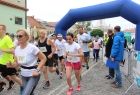 Zdjęcie przedstawia grupę biegnących osób, biorących udział w biegu ulicznym. W tle widoczna jest bramka startowa.