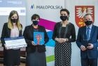 Marta Malec-Lech z zarządu województwa i Anna Mikosz radna wojewódzka wręczają promesę. W tle rollup z napisem Małopolska i herb Małopolski.