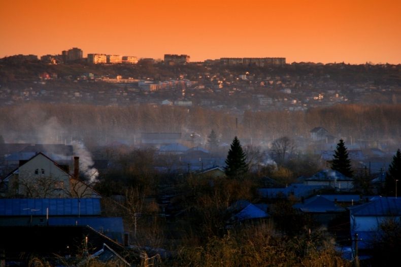 Widok na miasteczko, szary dym unosi się nad dachami domów, w tle, na dalekim planie widoczne osiedle