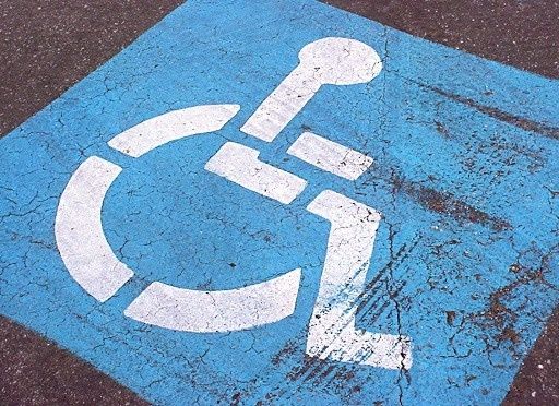 Znak dla osób z niepełnosprawnościami - na niebieskim tle widoczne białe kontury osoby siedzącej na wózku inwalidzkim.