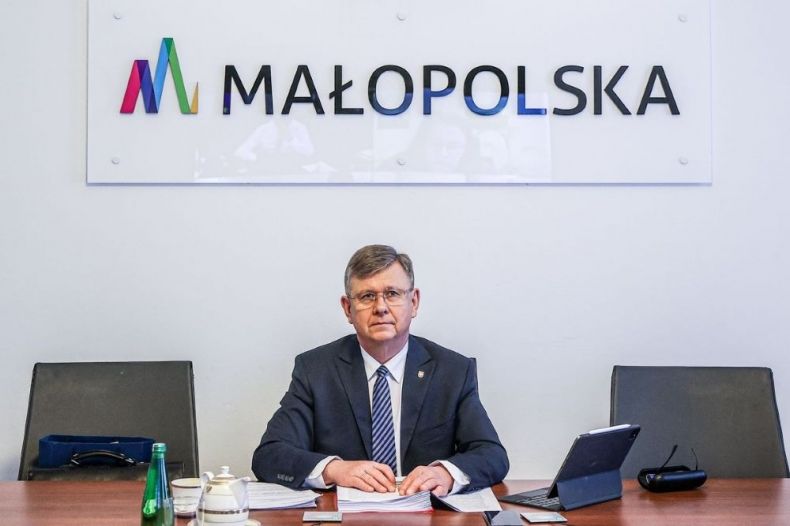 Marszałek Witold Kozłowski siedzi przy stole w sali konferencyjnej. Na ścianie napis Małopolska.