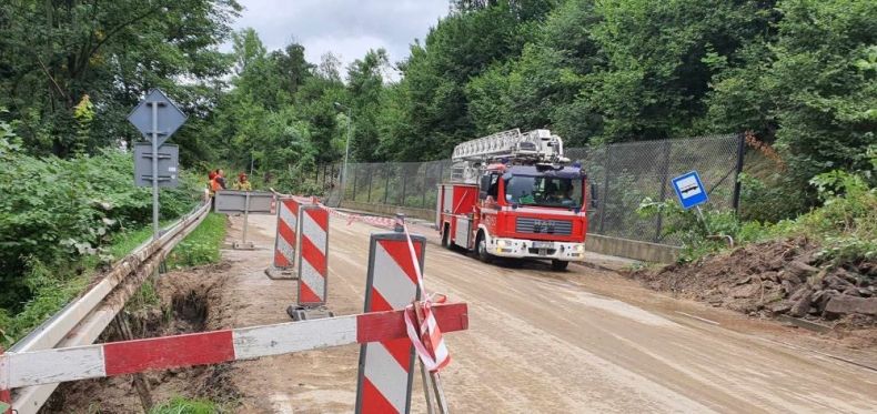 Wóz strażacki stoi na uszkodzonym fragmencie drogi. Widać ostrzegawcze pachołki.