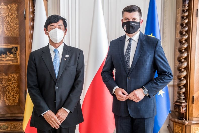 Wicemarszałek Łukasz Smółka stoi z Ambasadorem Japonii. Z tyłu widać flagi Małopolski, Polski i Unii Europejskiej.