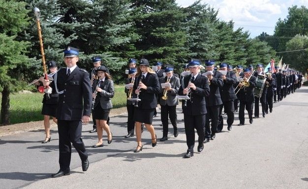 Orkiestra Dęta OSP we Włosani gra i maszeruje ulicą. W tle zieleń.