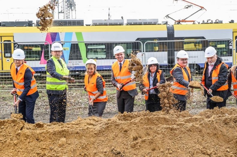 Wojewoda Małopolski Łukasz Kmita, wicemarszałek Łukasz Smółka oraz inni zaproszeni goście symbolicznie wbijają łopaty na budowie. Ubrani są w odblaskowe kamizelki i kaski na głowach.