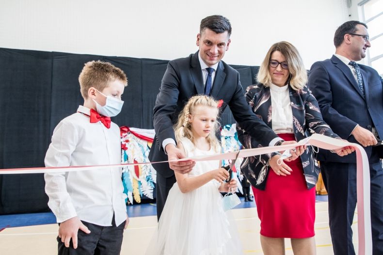 Wicemarszałek Łukasz Smółka przecina z dziećmi wstęgę.