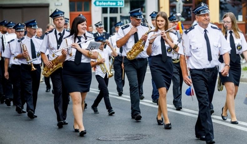 Orkiestra Dęta OSP w Tęgoborzy maszeruje ulicą i gra ubrana w strażackie mundury galowe.