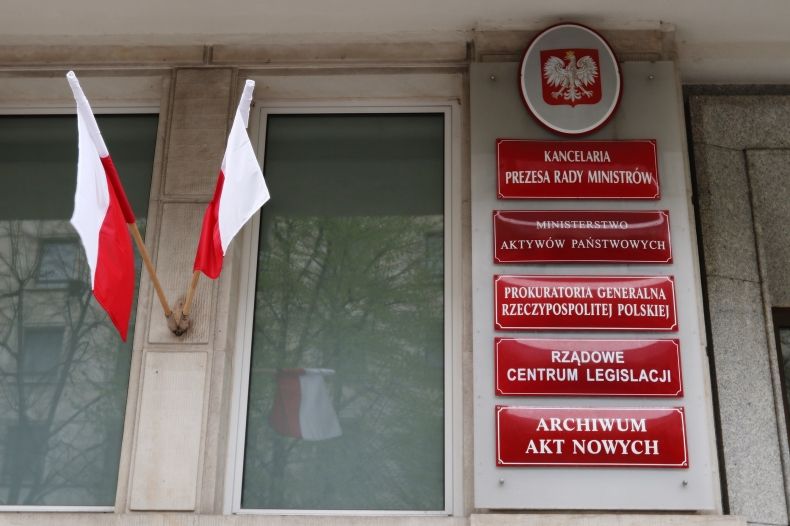 Tablice informacyjne przed Ministerstwem Aktywów Państwowych. Obok dwie flagi