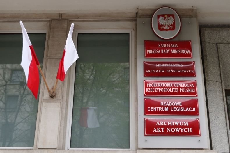 Tablice informacyjne przed Ministerstwem Aktywów Państwowych. Obok dwie flagi