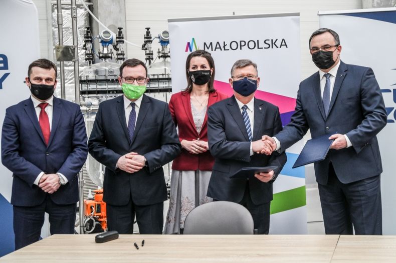 Grupa osób na tle bannerów Małopolski i Grupy Azoty Tarnów. Marszałek Kozłowski i prezes Hinc trzymają teczki z kopiami porozumienia