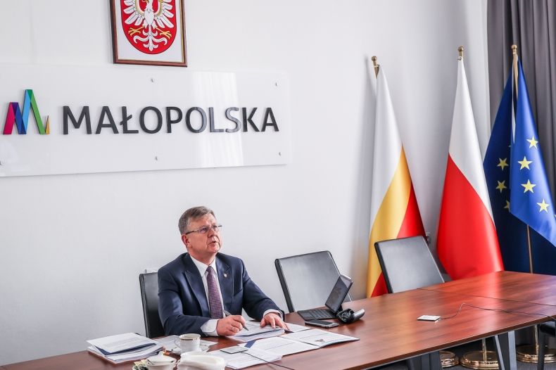 Marszałek Małopolski podczas posiedzenia zarządu, w tle napis MAŁOPOLSKA i flagi: krajowa, wojewódzka i UE