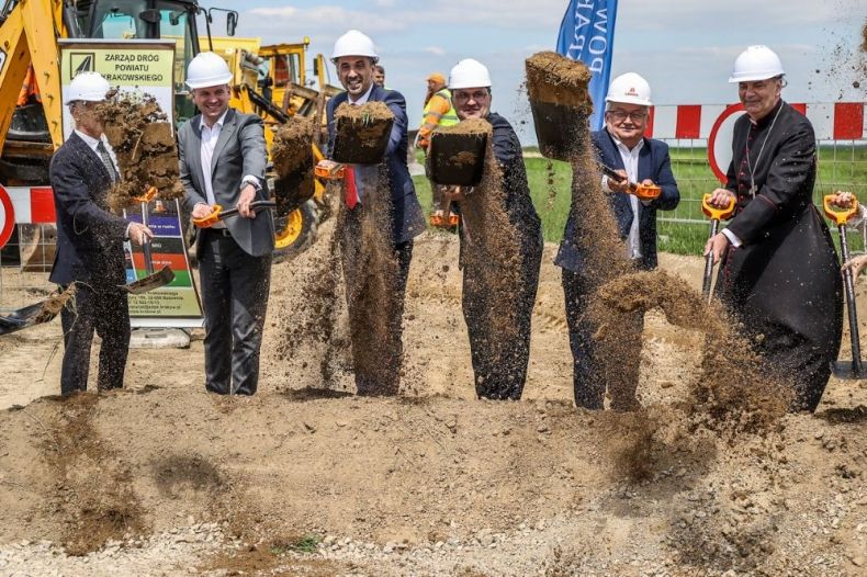 Wicemarszałek Łukasz Smółka z Ministrem Infrastruktury Andrzejem Adamczykiem i innymi uczestnikami wydarzenia wbija łopatę na placu budowy drogi.