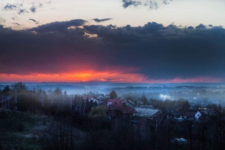 Widok na miasteczko spowite szarym dymem, w tle zachód słońca