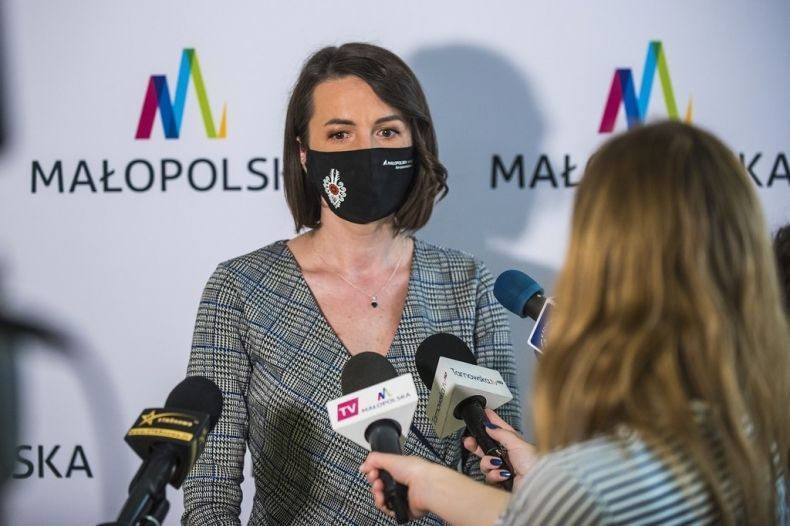 Marta Malec-Lech z zarządu województwa podczas konferencji prasowej wraz z dziennikarką przeprowadzającą wywiad. W tle widoczna ścianka z napisem Małopolska.