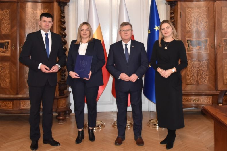 Marszałek Witold Kozłowski i wicemarszałek Łukasz Smółka stoją w gabinecie z nowym dyrektorem. Z tyłu widoczne zabytkowe meble i flagi Małopolski, Polski i Unii Europejskiej.